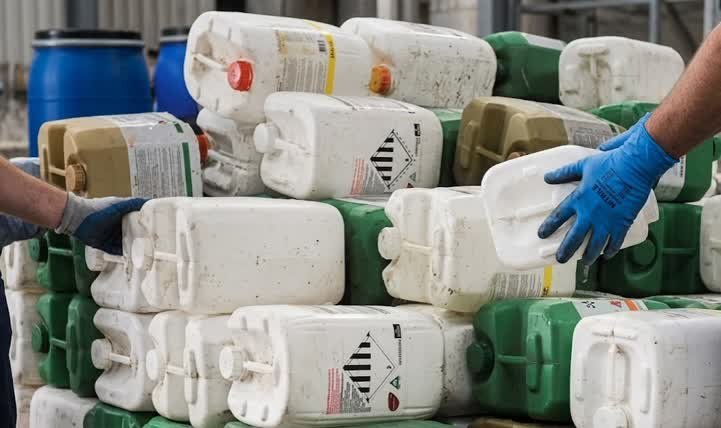Operario con guantes de protección manipulando envases químicos para una correcta gestión de residuos industriales en Kennedy.